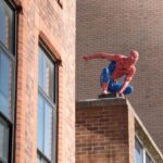 New Spider-Man Breaks North American Opening Weekend Box Office Record Spider-Man action figure crouching on a brick ledge of a building behind tall windows.