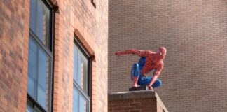 Spider-Man action figure crouching on a brick ledge of a building behind tall windows.